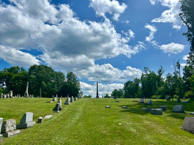 A broad mown cemetery lawn with scattered markers and distant monuments.