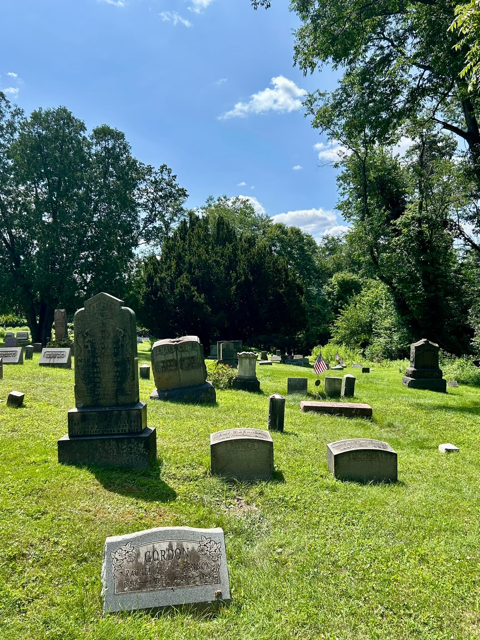 Headstones on a sunny Henderson Cemetery lawn with a flag